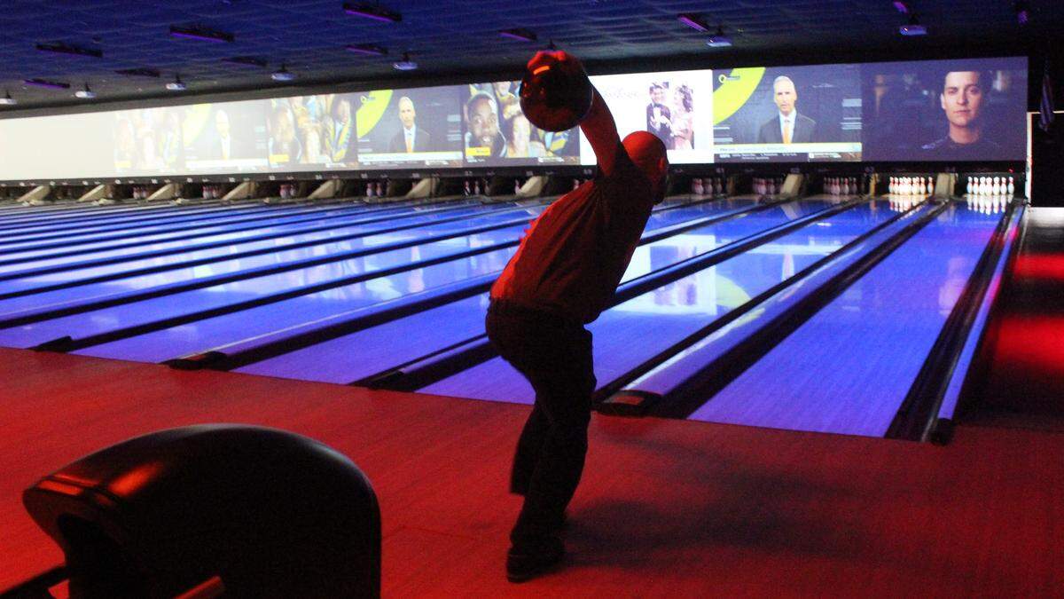 Jared Zimmerman bowls in one of of the blacklight-lit lanes at Bowlero, while Tobey Maguire appears to watch from a video screen.