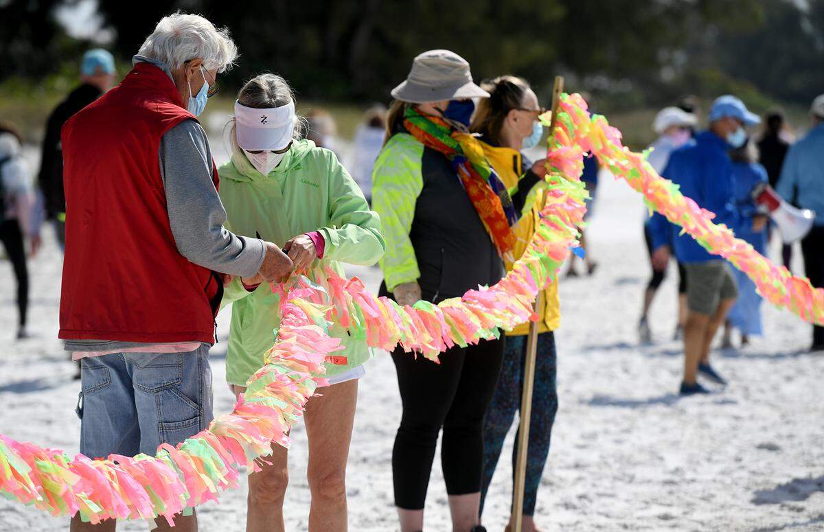 02/16/21--A group of people led by Cathy Tobias hold a memorial created from ribbons and stretching 250 yards to remember the almost 27,000 people lost to COVID-19 in Florida.