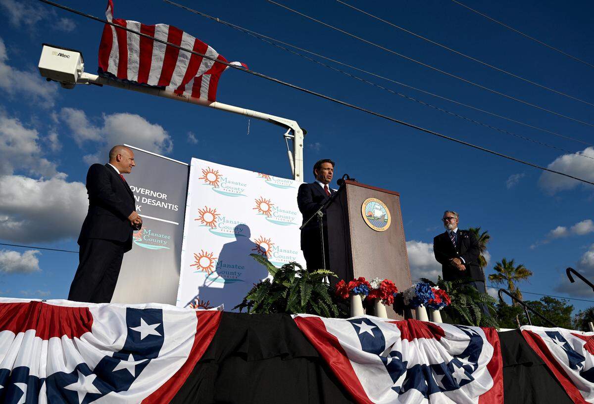 Florida Gov. Ron DeSantis addresses a gathering with Manatee County Commissioners Kevin Van Ostenbridge and Mike Rahn in Manatee County for the opening of a park named in his honor on Wednesday, Oct. 18, 2023.