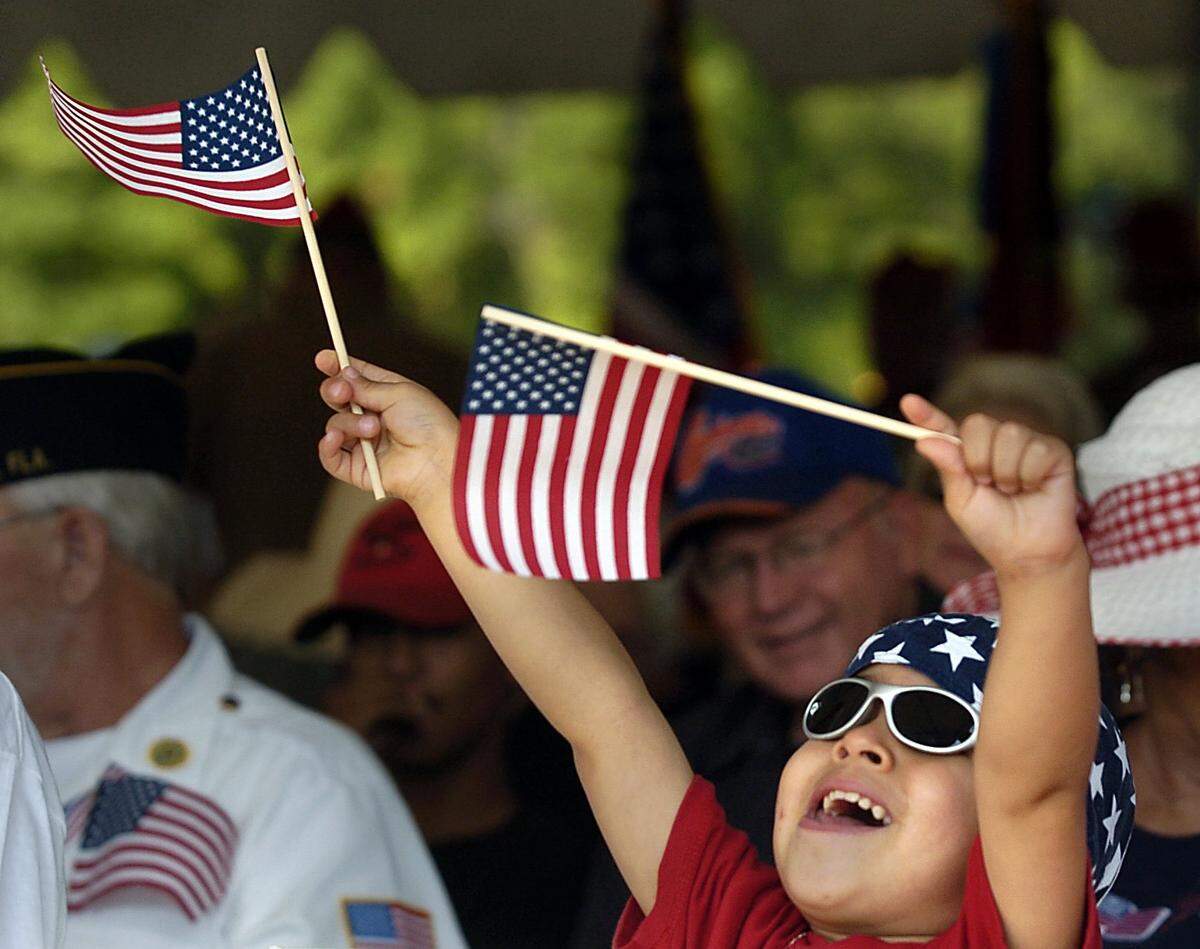 Matthew Roig, 3, plays with his American flags as his sister participates in the Memorial Day 2006 service at Sutton Park in Palmetto.
