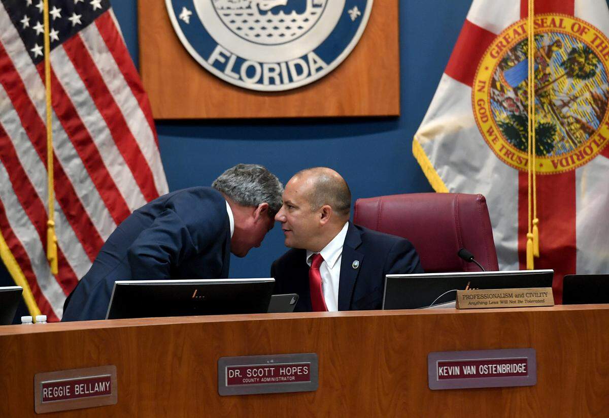 County Administrator Scott Hopes leans in to listen to Commissioner Kevin Van Ostenbridge at a meeting where a vote on Hopes’ contract renewal was approved on May 24, 2022.