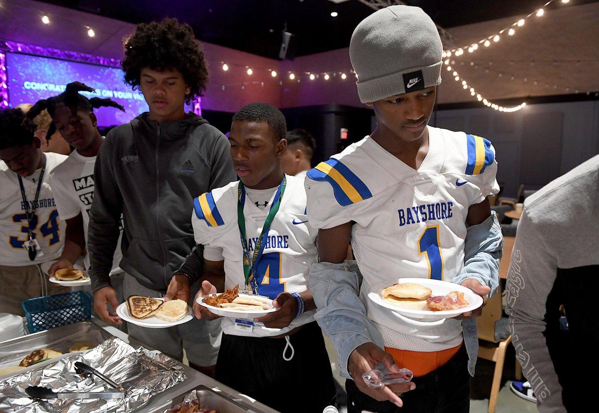 Bayshore High football players load up their plates with pancakes, bacon, fruit and vegetables at Church of the Cross, which prepares a pregame meal for them.