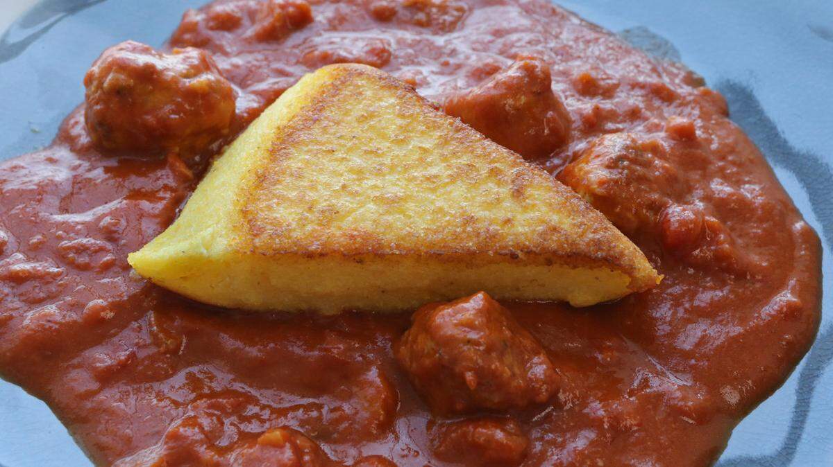 Polenta wedges are served on sausage in a tomato sauce. TNS