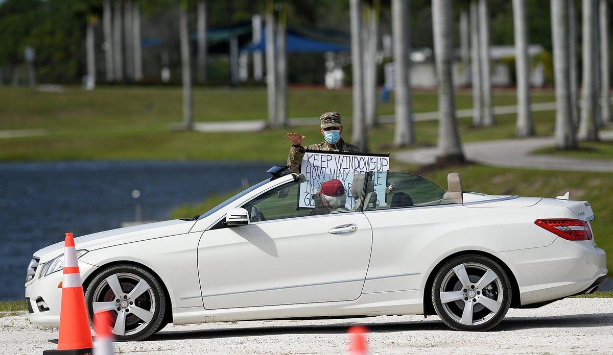 A member of the National Guard holds a sign saying ‘keep windows up’ as he gestures for a driver to close their convertible top in line for coronavirus testing at the UTC Mall.