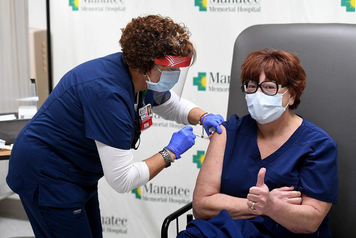 12/23/20--Manatee Memorial Hospital nurse Merrily Moran gives an injection of the Moderna vaccine to fellow nurse Joanne Nipper as the hospital began vaccinating front-line caregivers in December.