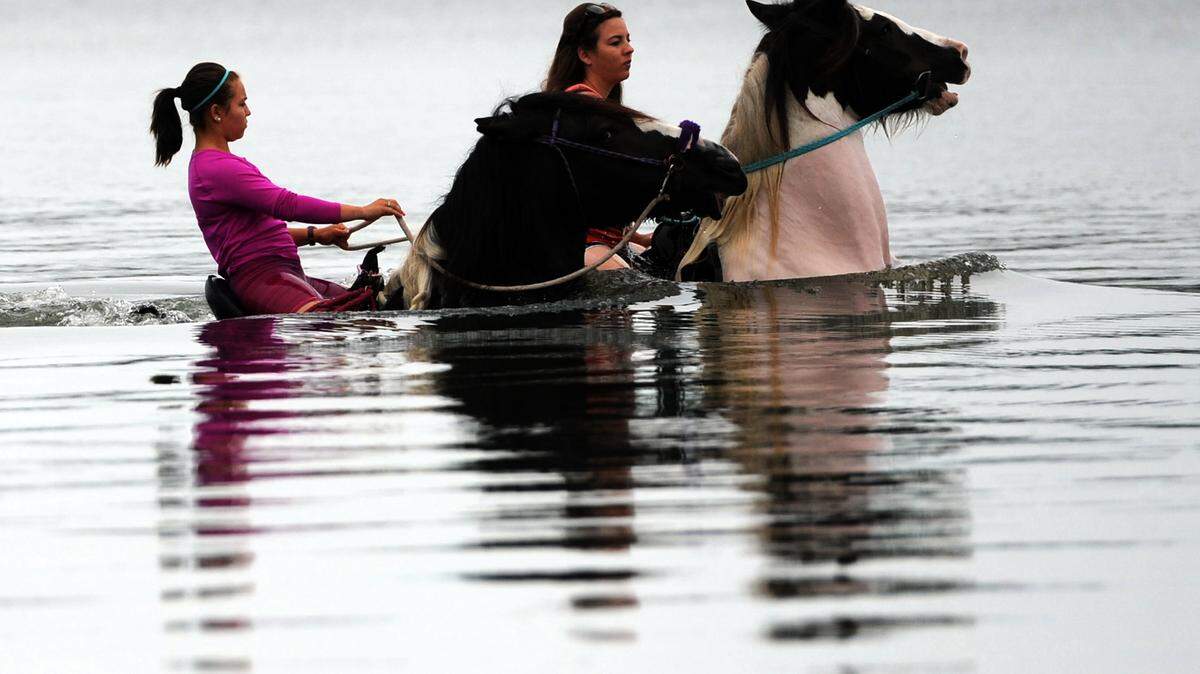 Mercedes Pages, a guide with C Ponies, Myakka City, and rider Kristin Burns, are reflected in the calm waters as they ride horses Thursday in Palma Sola Bay.GRANT JEFFERIES/Bradenton Herald
