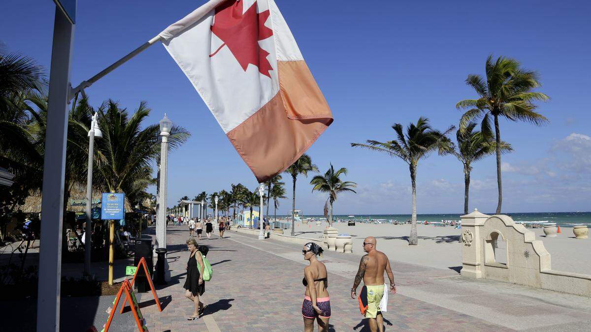 In this Monday, Nov. 23, 2015 photo, a Canadian flag flies as people walk along the boardwalk in Hollywood, Fla. Visits by the United States' largest supply of international visitors from Canada are expected to be down by 8 percent this year due to the weak Canadian dollar. (AP Photo/Lynne Sladky)