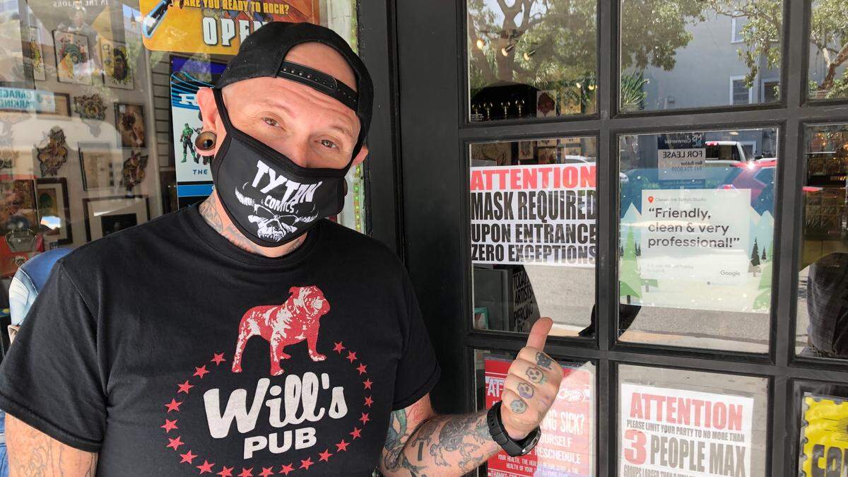Ty Harris, owner of Tyton Comics, 306 12th St. W., points to a sign at his business’ entrance requiring customers to wear a mask.