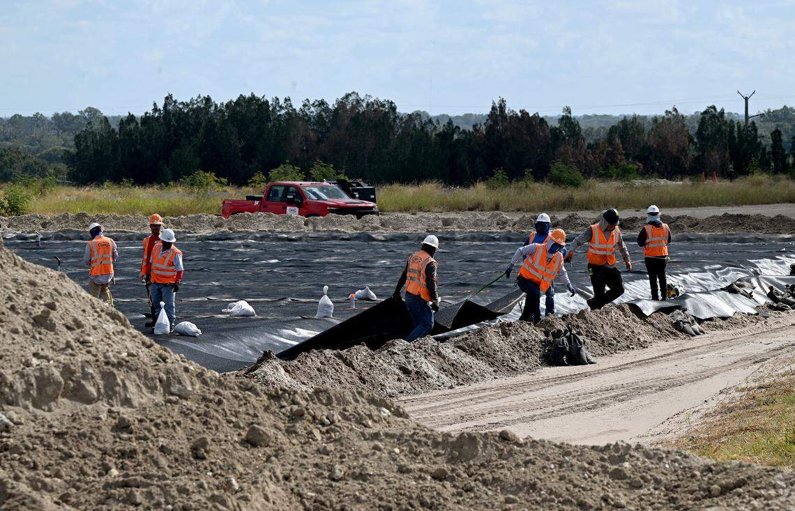 Workers pull a liner across the dirt of Old Gypsum-Stack North where large geo-tubes will be set up in the future to drain water from solids dredged from New Gypsum-Stack South. Site operators at Piney Point recently announced a milestone achievement with the closure of the Old Gypsum Stack-South compartment, one of four ponds that need to be closed at the former phosphate processing plant.