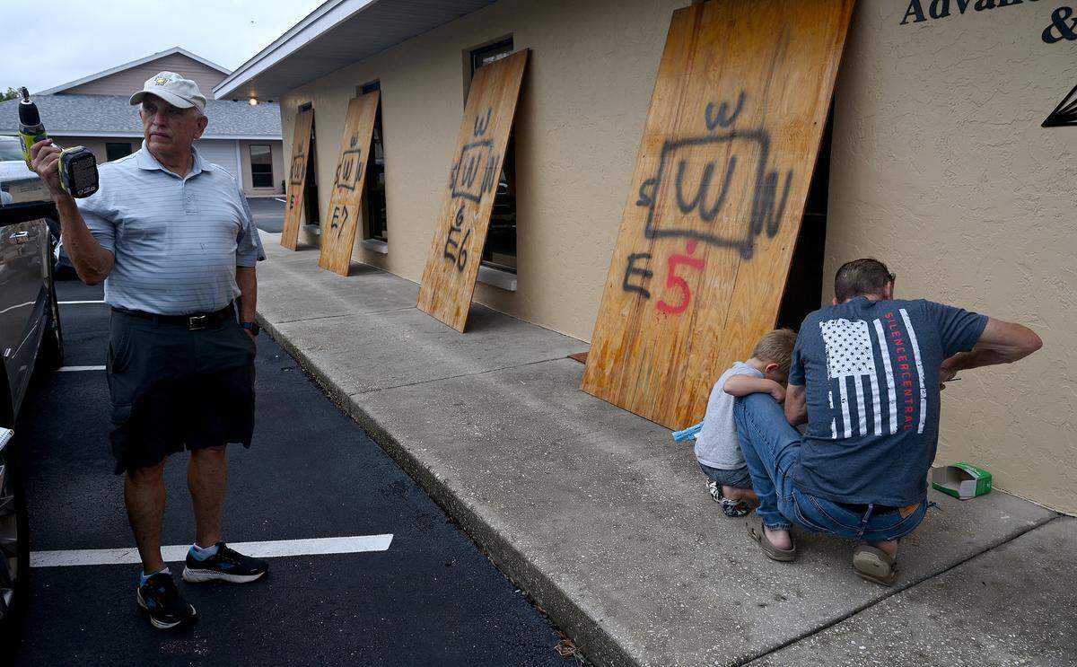 Dr. J. Terry Alford with friends Paul Connors and Branson Ellard, 4, help board up Alford’s West Bradenton business as Hurricane Milton approaches Manatee County on Oct. 7, 2024.