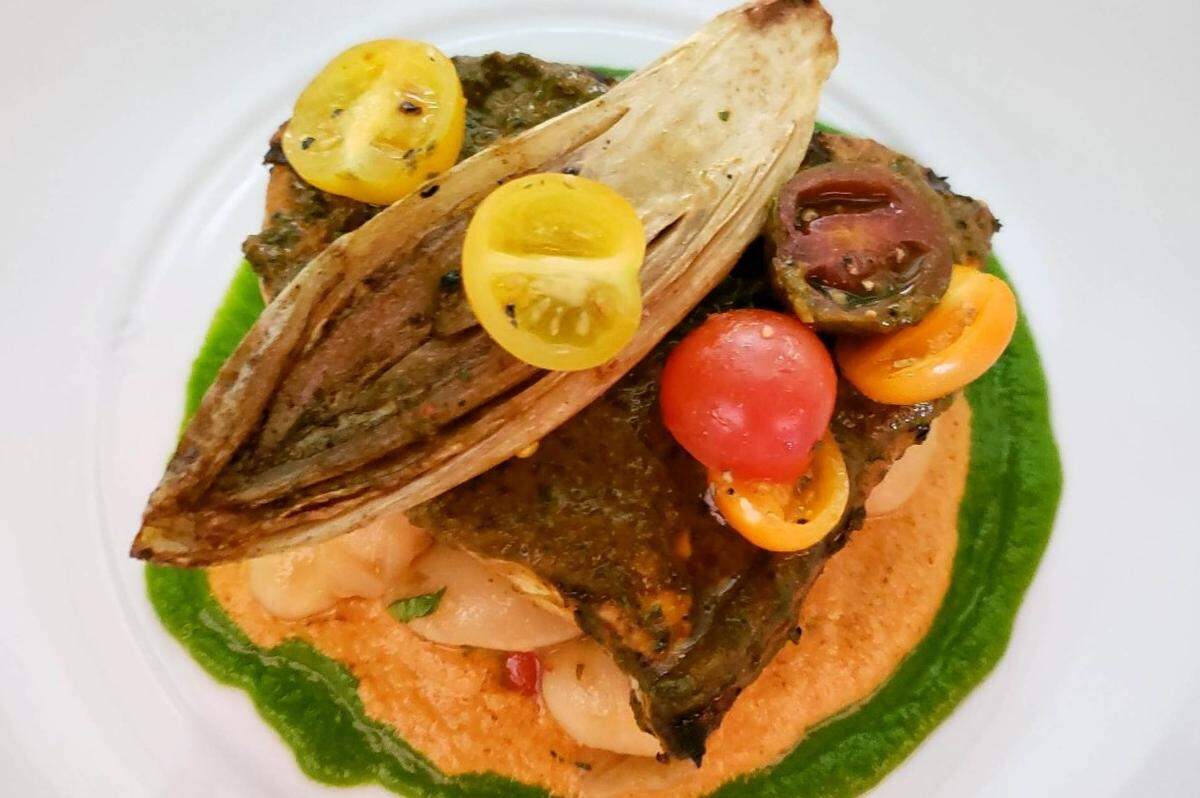 The Chermoula-Grilled Atlantic Swordfish Steak is served with fennel and gigante bean pickled salad, almond romesco sauce, and pan seared Belgian endives.