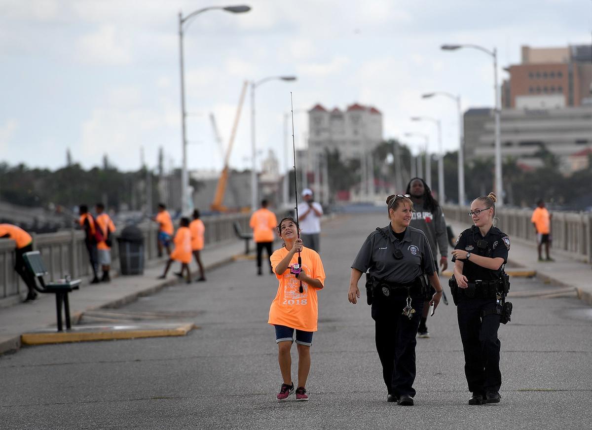 Yarellis Martin, 13, walks with Bradenton police officers Scottie Camacho and Kristie Affolter after catching two sharks during the Manatee Bridging the Gap 2018 Youth Fishing Tournament on the Green Bridge in Palmetto Thursday morning.