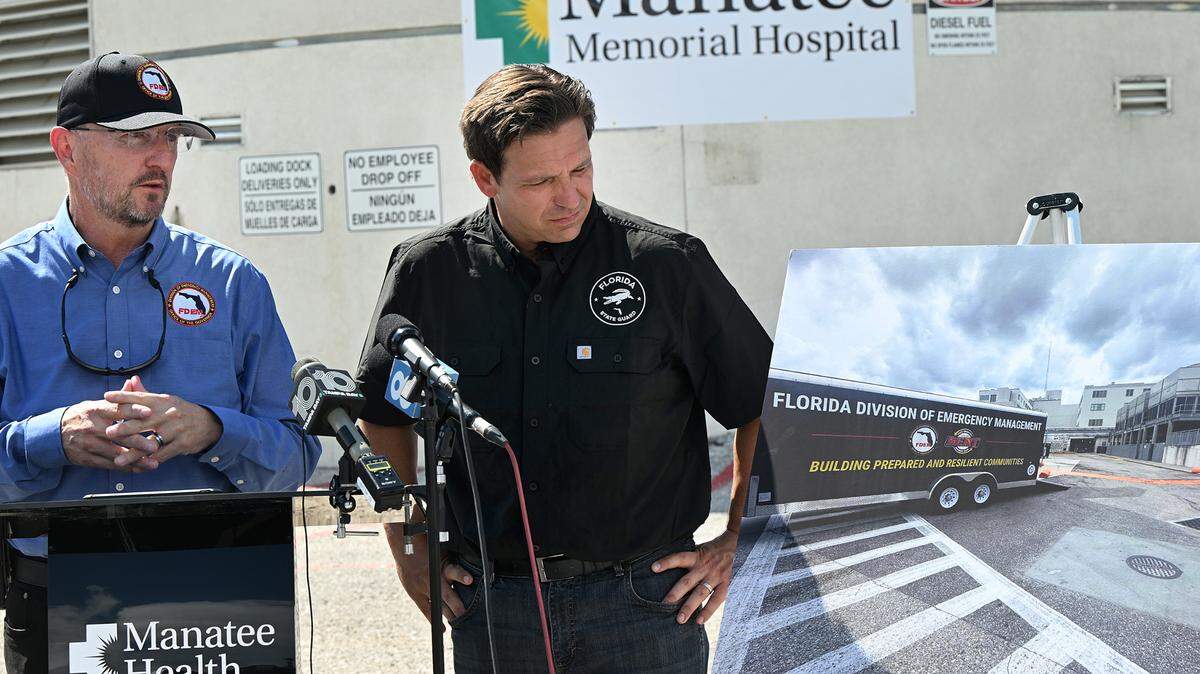 Florida Gov. Ron DeSantis looks at a photo of the FDEM deploying a Tiger Dam at Manatee Memorial Hospital where he spoke at a press conference with FDEM Dir. Kevin Guthrie, left, on Monday, Sept. 30, 2024. Florida Division of Emergency Management deployed a Tiger Dam around sections of the hospital before the arrival of Hurricane Helene.