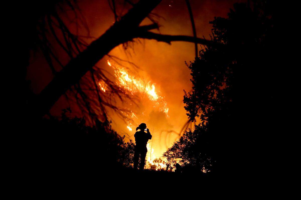 A firefighter takes a cell phone picture during a wildfire Saturday, Dec. 16, 2017, in Montecito, Calif. The so-called Thomas Fire is now the third-largest in California history.