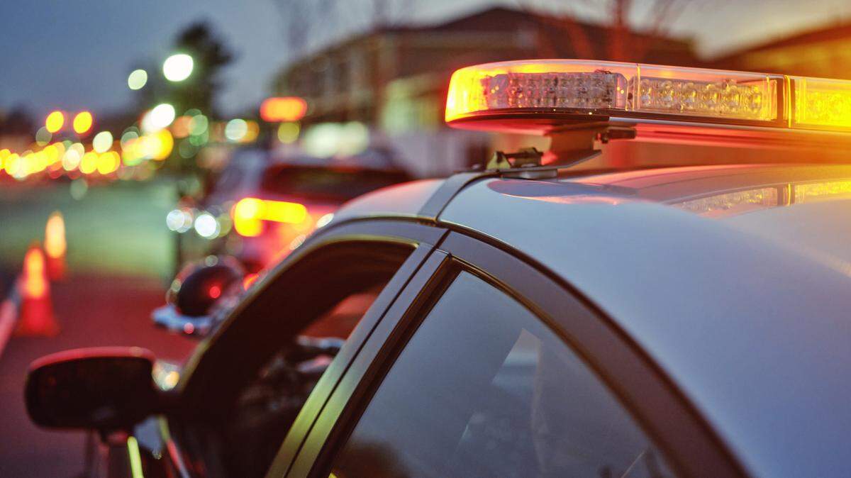 A police car at night alongside a road with emergency lights flashing.