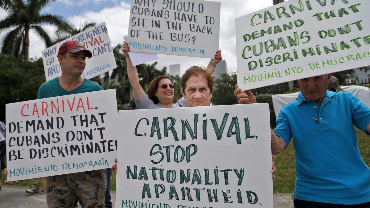 FILE- In this April 12, 2016 file photo, Victor Garcia, of Miami, from left, Maria Hernandez and Miriam Dominguez, protest against Carnival Corporation as they hold a rally in Doral, Fla. Two Cuban-American men are asking a Miami federal judge to guarantee they and other Cuban exiles will not suffer discrimination on upcoming Carnival Corp. cruises to Cuba. A hearing was held in Miami, Thursday, April 21, 2016. (Carl Juste/The Miami Herald via AP, File) MAGS OUT; MANDATORY CREDIT
