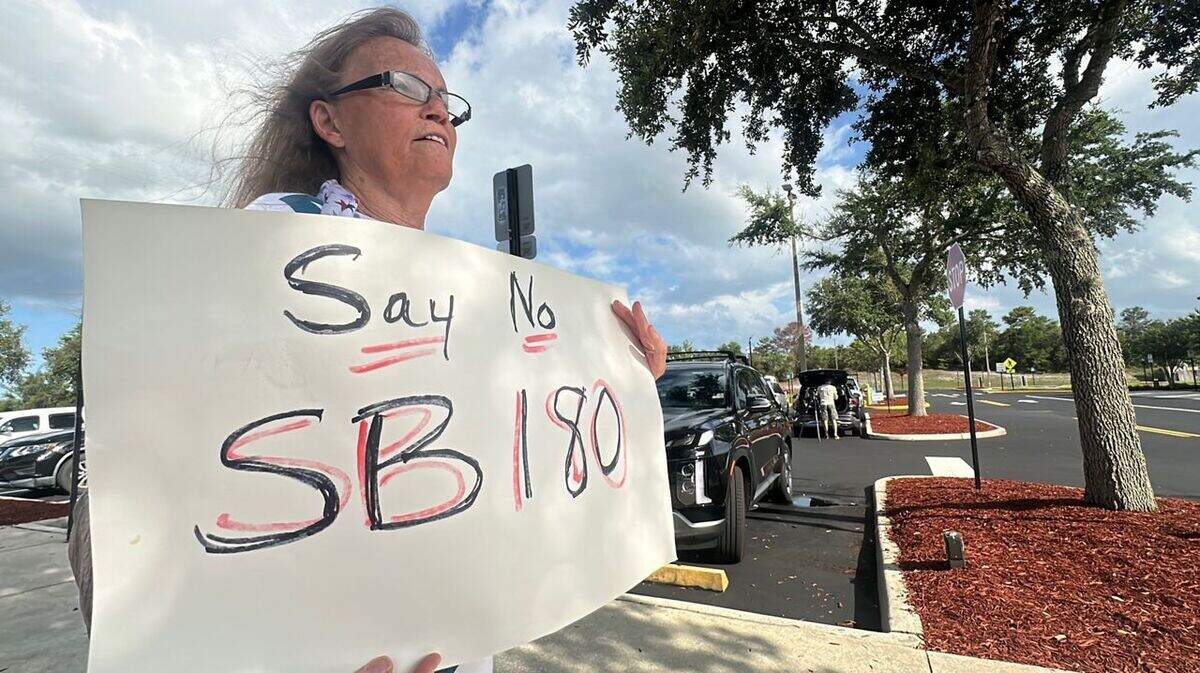 Deltona, Florida, resident Stephanie Cox held a sign that said, “Say No to SB 180“ ahead of a Deltona City Commission meeting in June where officials approved a residential development moratorium in defiance of the new state law. Deltona is one of the cities that joined a lawsuit against Senate Bill 180.