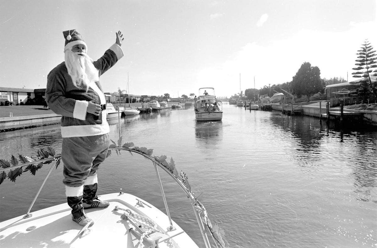 Santa Claus waves from the deck of a boat in a residential boat canal, 1980.