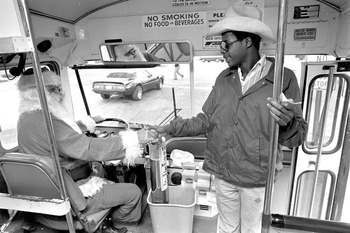 A bus rider is greeted by Santa Claus, who is driving the city bus for the Christmas holidays from the main bus depot at the County Courthouse, 1980.