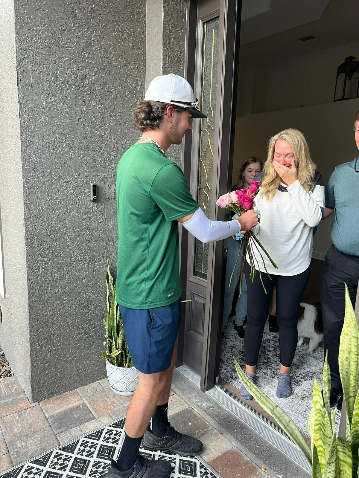 Christine Orlander holds a hand over her mouth in surprise as she has been given pink roses by a member of the Lakewood Ranch High School varsity baseball team on March 3, 2022. She recently had double mastectomy surgery and has been recovering at her Lakewood Ranch home.