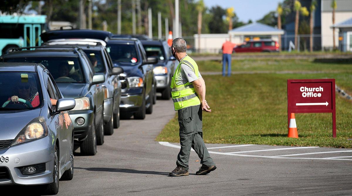 12/16/20--Volunteer Mac Aldrich directs cars as other volunteers help sort, bag and load food into the cars of those in need at the Fifty Third Avenue Church of Christ.