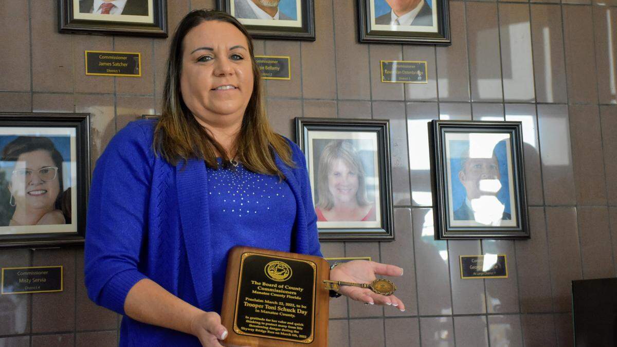 Florida Highway Patrol Trooper Toni Schuck poses with a ceremonial plaque and a key to the city of Bradenton on Tuesday, March 22, 2022, which the Manatee Board of County Commissioners declared “Toni Schuck Day” after she used her FHP vehicle to prevent a deadly crash during the annual Skyway 10K race on March 6, 2022.
