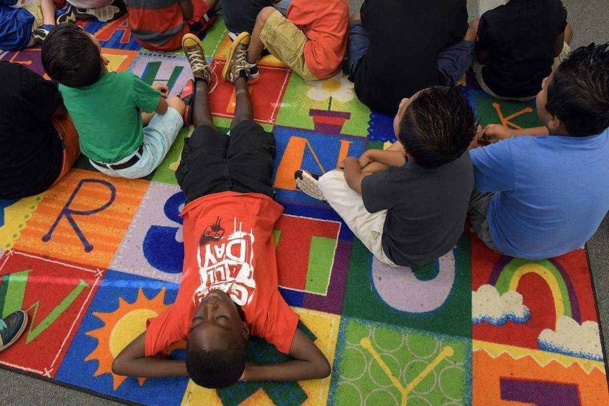 Young boys sit and lie upon a rug to read a book at Visible Men Academy, where officials are hoping to teach boys from low-income families character traits and move their academics up the scale. File photo
