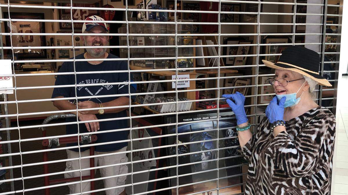 Monica Norman, owner of the El Gaucho food store, and John Petrovic, owner of Legends in Sports, chat through the grates of his security wall at DeSoto Square mall, which began reopening on Monday.