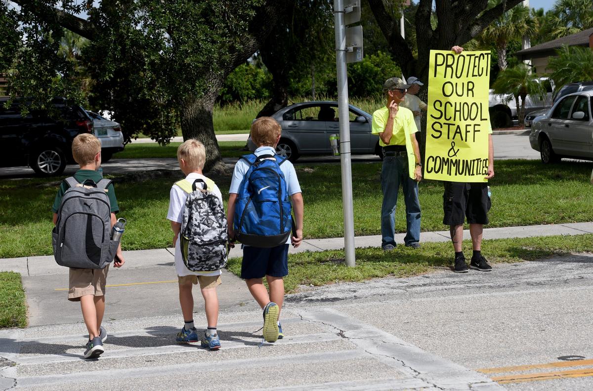 Students cross the street as around 20 people showed up outside Kinnan Elementary School at dismissal time Monday to hand out fliers and hold signs against the construction of a communications tower close by.