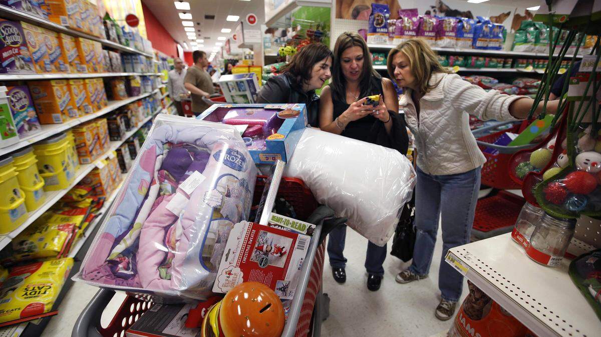 FILE - In this Nov. 28, 2014 file photo, Target shoppers Kelly Foley, left, Debbie Winslow, center, and Ann Rich use a smartphone to look at a competitor's prices while shopping shortly after midnight on Black Friday, in South Portland, Maine. Americans are expected to spend at a slower pace than last year during the crucial winter holidays, weighed down by sluggish wage growth and other factors, according to a forecast Thursday, Oct. 8, 2015, from the National Retail Federation. (AP Photo/Robert F. Bukaty, File)