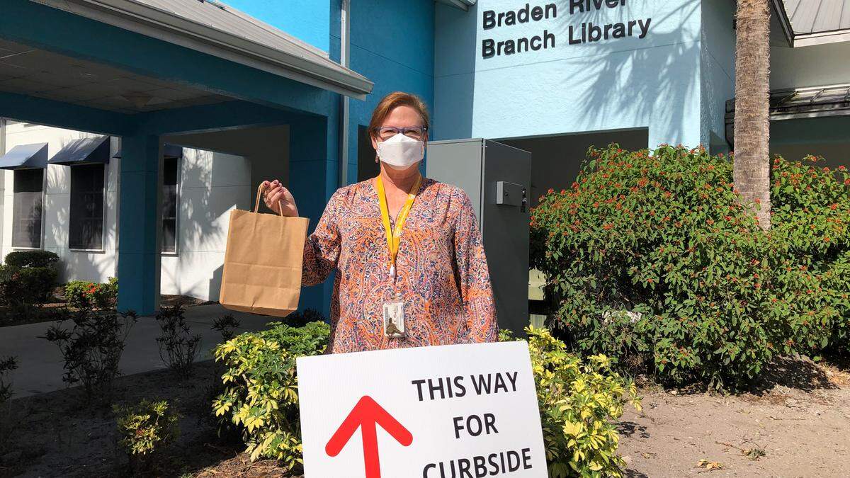 5/21/2021--While Braden River Branch Library will be closed to walk-in visitors for expansion and renovation construction, patrons can still take advantage of curbside service. Mary Frueh, assistant library supervisor, shows how library staff will deliver items to drivers on the east side of the library.