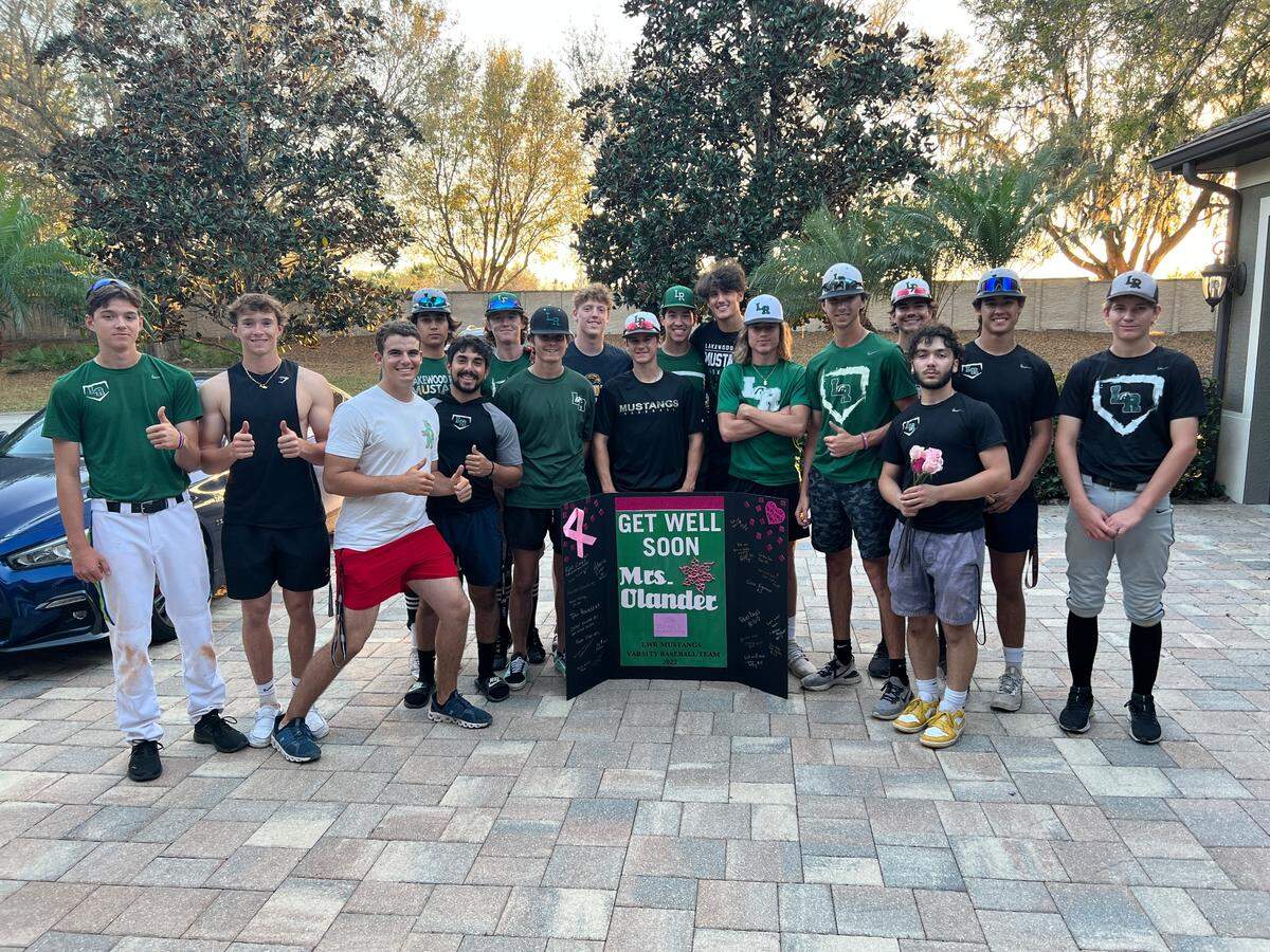 Members of the Lakewood Ranch High School varsity baseball team stands in Christine Olander’s driveway holding pink roses and a “Get well soon” card on March 3, 2022. Olander recently had double mastectomy to fight breast cancer and has known some of them since they played Little League baseball with her son.