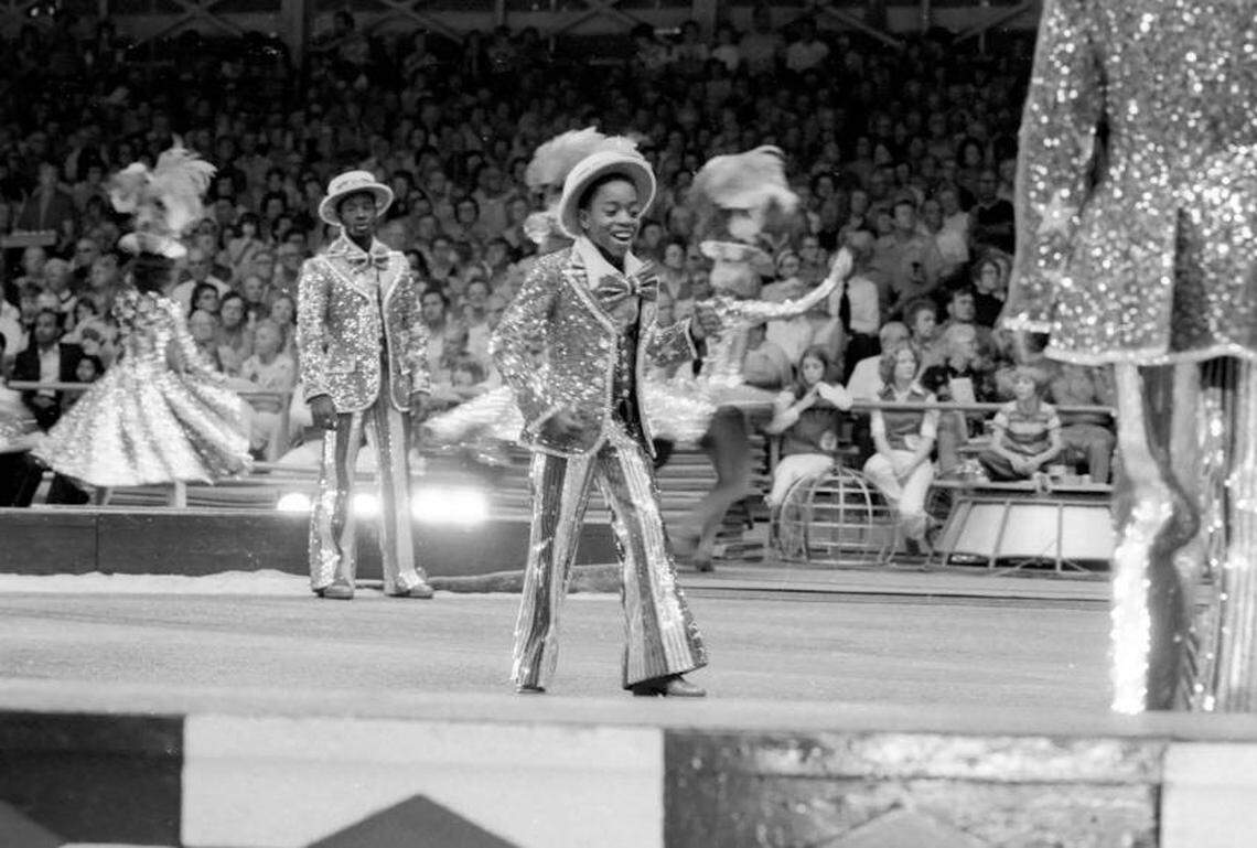 Children and adults dance and perform in the ring for a large crowd in 1976.