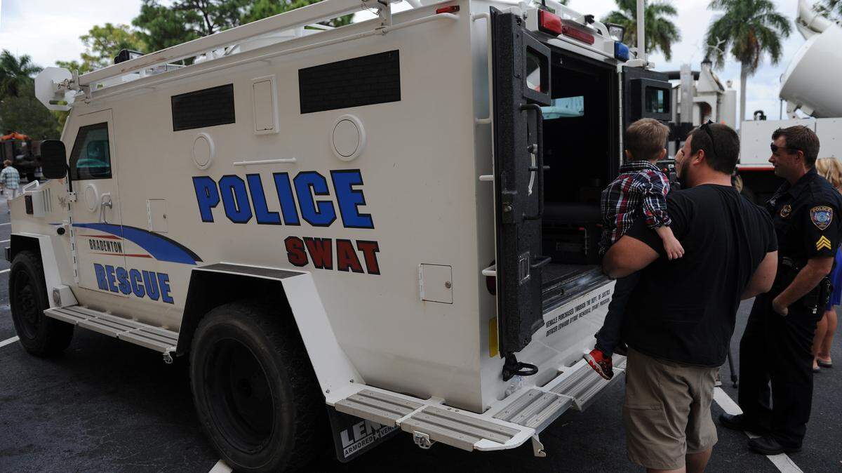 Charles Hoefling holds his son, Michael, 4, as they look at an armored truck used by the Bradenton Police Department SWAT team. It was one of the trucks on display at the Touch-a-Truck event Saturday at the Manatee County Central Library. 
 GRANT JEFFERIES/Bradenton Herald