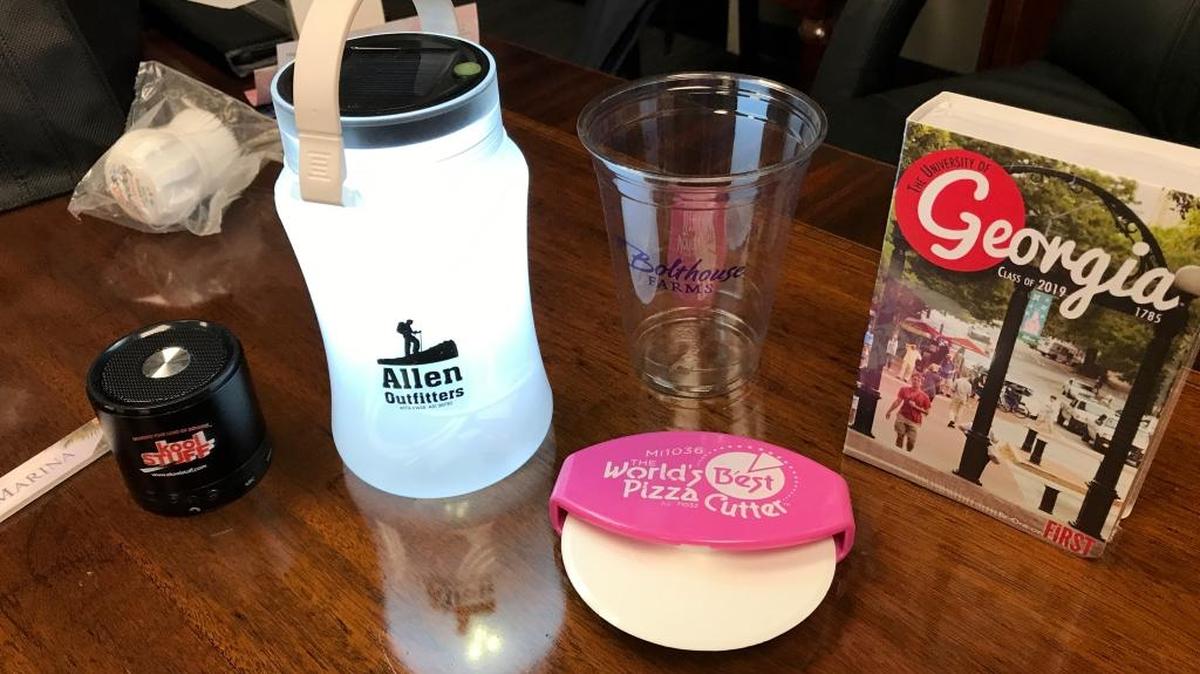 Kool Stuff promotional items include, from left. a fingernail file, Bluetooth speaker, solar-powered emergency light, plastic cup, and box containing sunglasses.