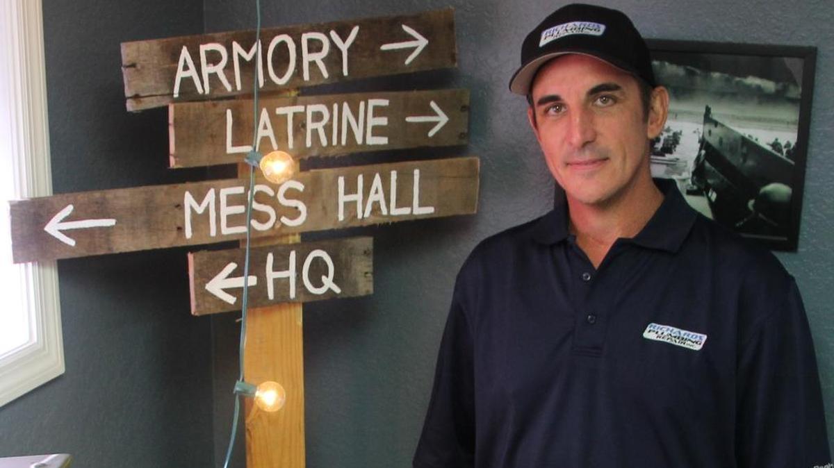 Richard Krause stands in the war room at Richards Plumbing Repair. The signs, pointing to the fictional latrine and mess hall, hint at his sense of fun.