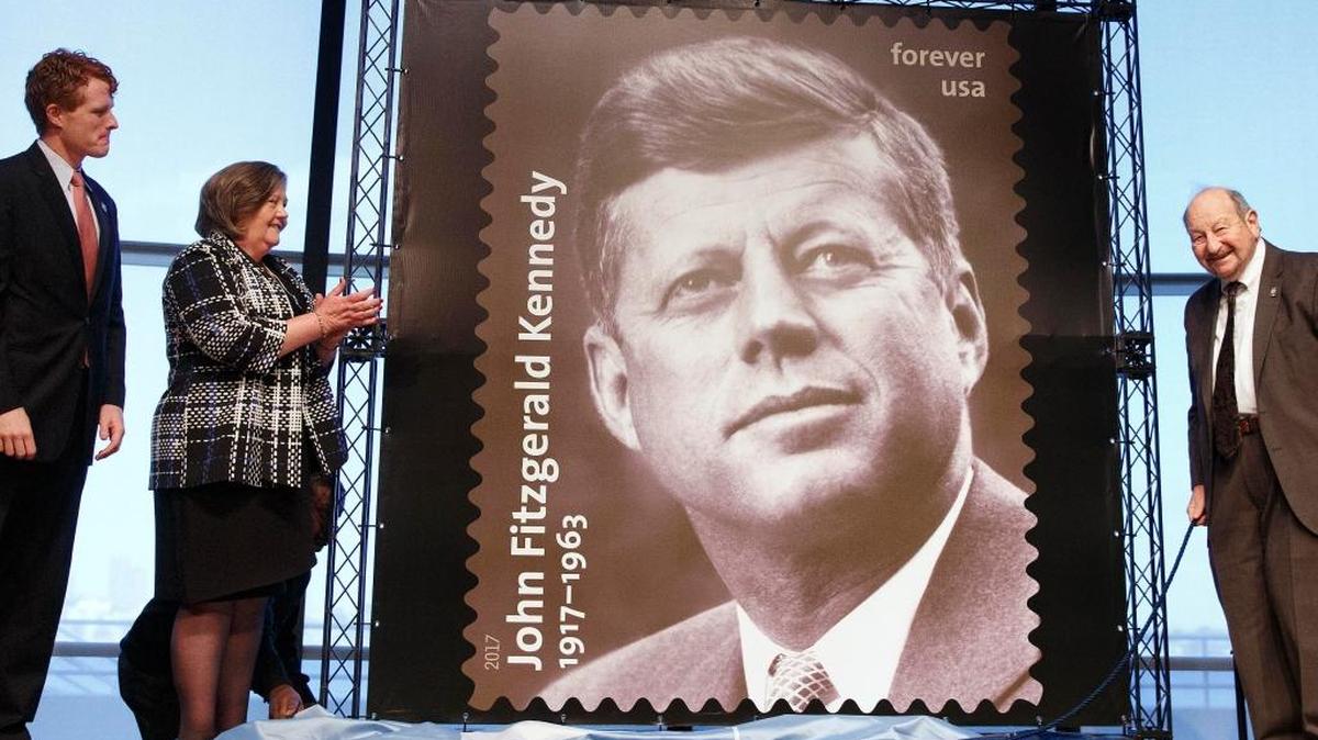 Rep. Joseph P. Kennedy III, D-Mass., left, Postmaster General Megan Brennan and photographer Ted Spiegel unveil the John F. Kennedy Centennial Stamp on Monday at the John F. Kennedy Library in Boston.