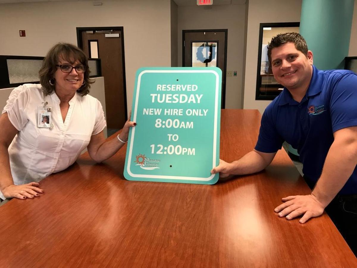 Julie Bassett, human resources manager, and Joe Spain, talent acquisition, hold a sign reserved for new hires attending their initial training session at Manatee County Government. They will need to use the sign many times in 2018 to keep up with the county’s staffing requirements.