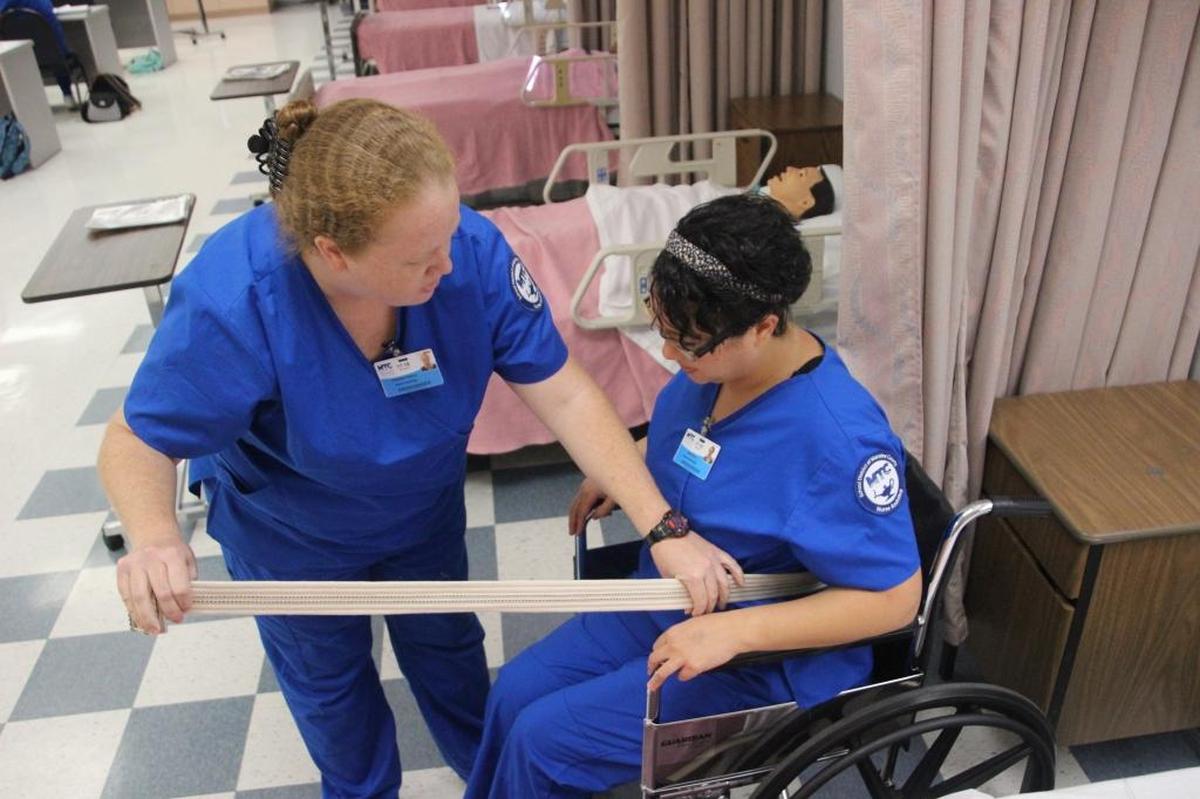 Elizabeth Chancey, left, and Julia Buono, who are studying to become certified nursing assistants at Manatee Technical College, work on an exercise that teaches them how to help patients get out of bed and into a wheelchair.