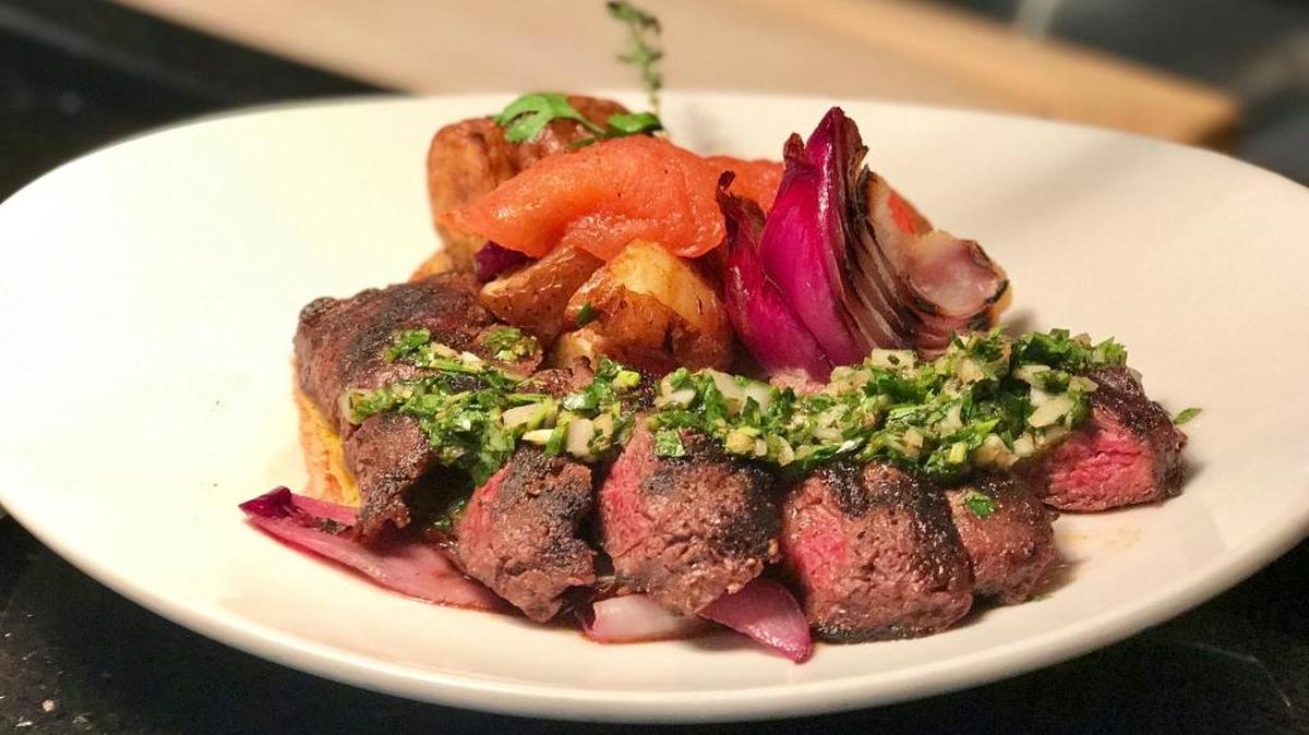 The Churrasco de Entraña con Chimichurri, an Argentinian dish starring on the Michael’s on East Epicurean Adventure menu, has grilled skirt steak with chimichurri, grilled red onions, roasted roma tomatoes and crispy red bliss potatoes.