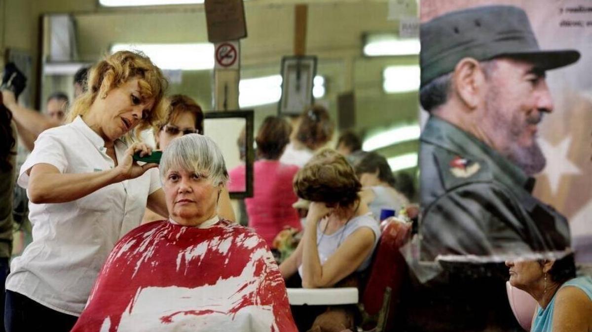 Josefina Hernandez cuts a customer’s hair next to a poster of Fidel Castro hanging in a barber shop in Old Havana. In 2010, Cuba began turning over some formerly state-run barber shops and hair salons to the employees who work in them.