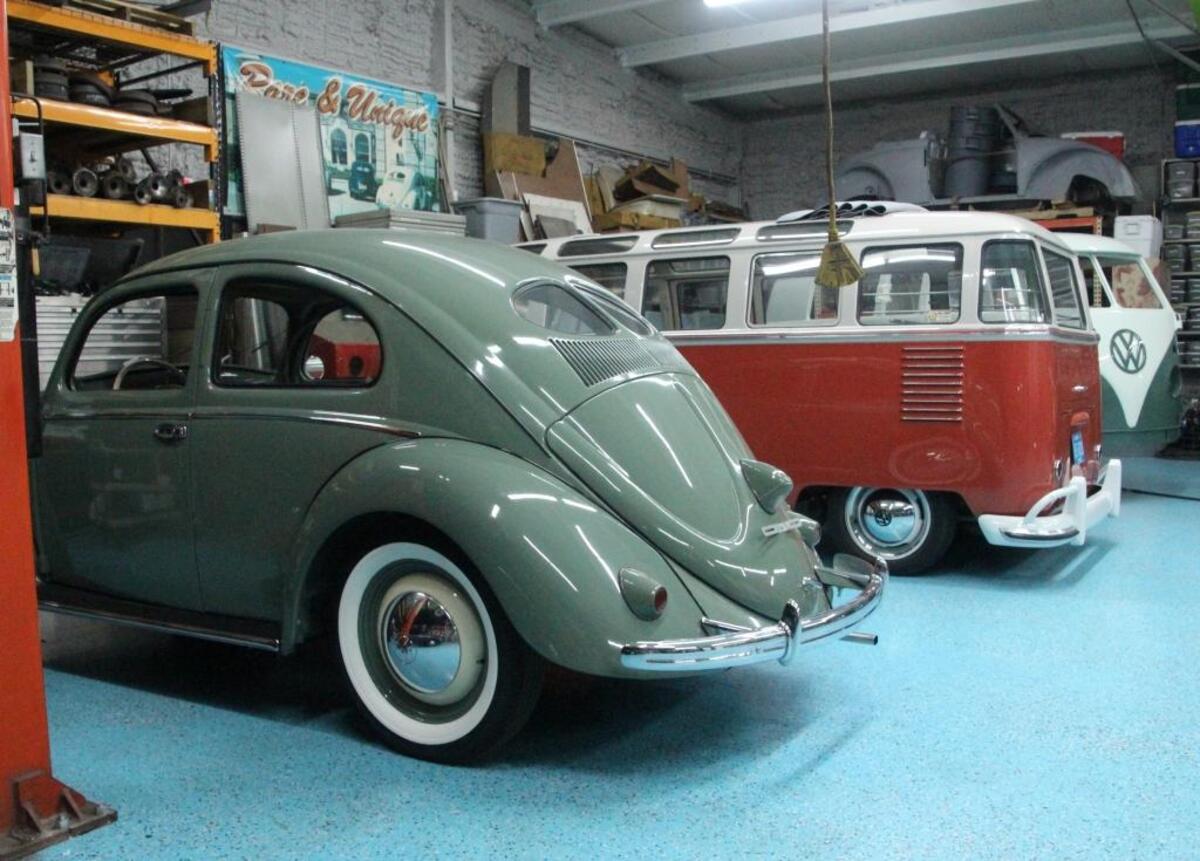 Two very rare and expensive Volkswagens, a split window Beetle and a 23-window bus, are parked side-by-side at Rare and Unique Restoration.