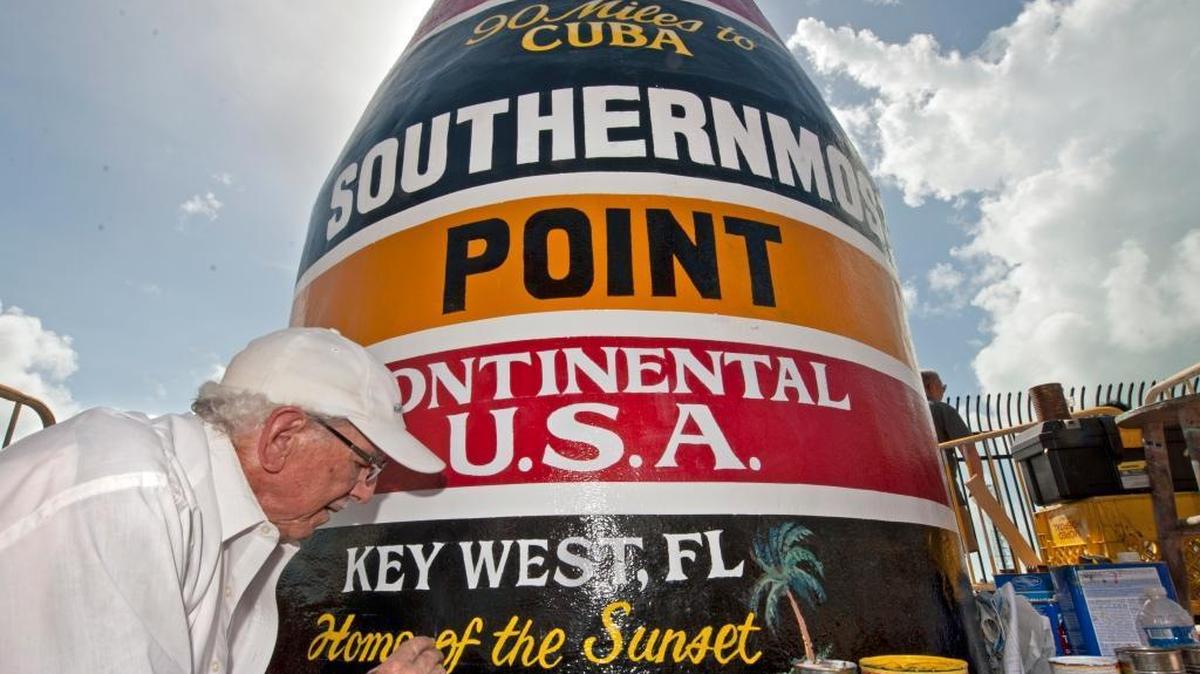 In this photo provided by the Florida Keys News Bureau, artist Danny Acosta completes lettering the Key West buoy, which reads, “90 Miles to Cuba. Southernmost Point in the Continental U.S.A., Key West, FL,’’ on Monday, Oct. 23, 2017. Hurricane Irma pummeled one of the most-photographed tourism icons in the Florida Keys on Sept. 10, 2017, stripping most of the paint and a large chunk of stucco.