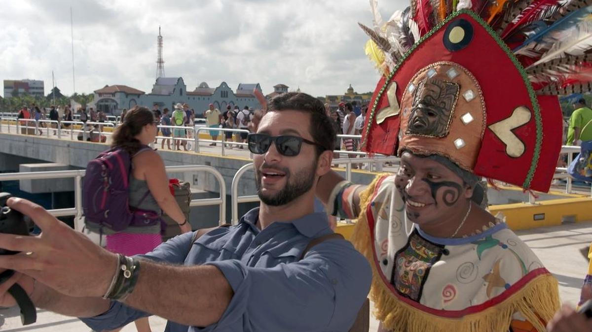 Josh Garcia takes a selfie with a resident of Playa del Carmen, Mexico, dressed in costume to greet cruise passengers in a scene from a new show airing on NBC this fall called “The Voyager with Josh Garcia.” The show is one of three new shows produced by Carnival Corp., showcasing vacation and travel connected to cruising.