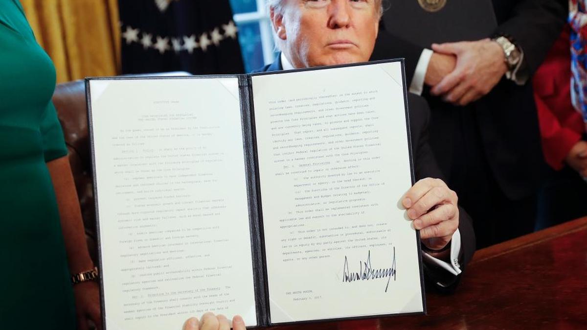 President Donald Trump holds up an executive order that will direct the Treasury secretary to review the 2010 Dodd-Frank financial oversight law, which reshaped financial regulation after 2008-2009 crisis.