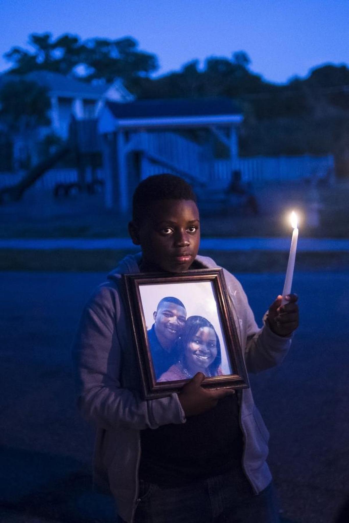 Zakai Cherenfant, 11, holds a picture of his deceased step-father, Dequan Randolph and his mother, Rosemary Randolph, during a candlelight vigil for Dequan Randolph on Thursday evening, November 10, 2016 in Bradenton. Family and friends gathered for a memorial to Randolph, who was killed on Thursday, November 3, at the site of the shooting to share prayers and memories.