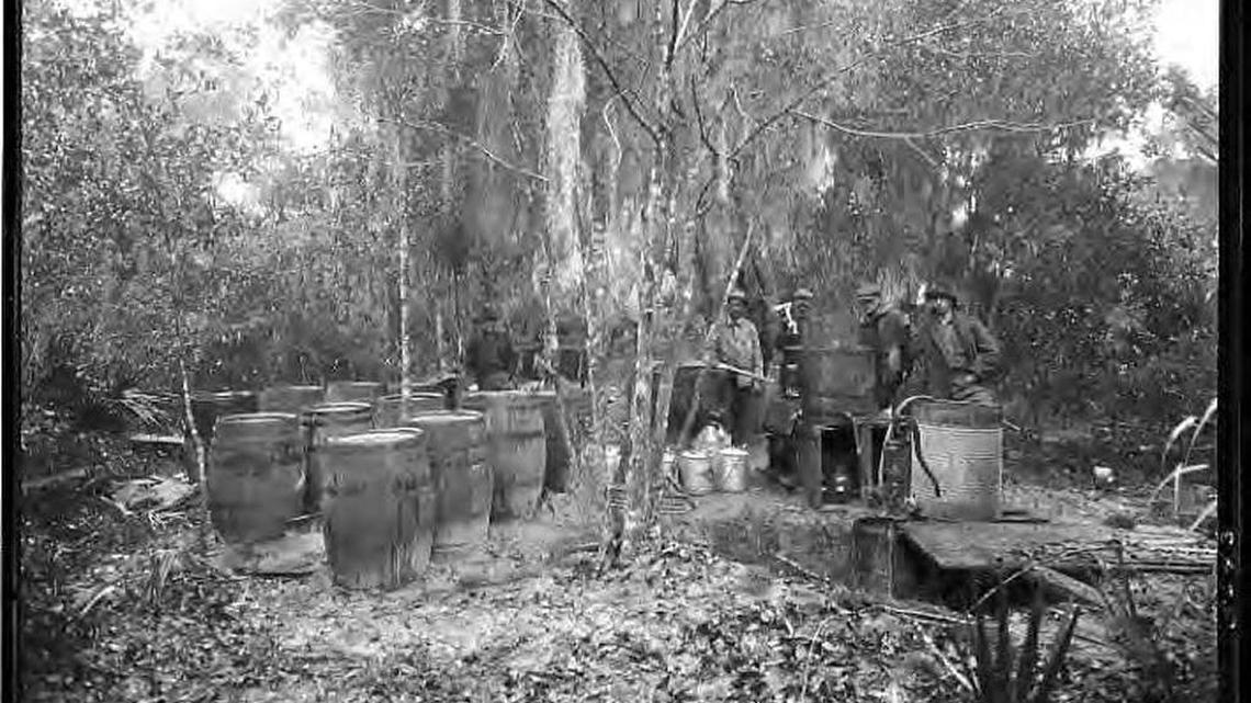 Armed men stand beside moonshine still, jugs and barrels in the woods near Riverview in 1920.