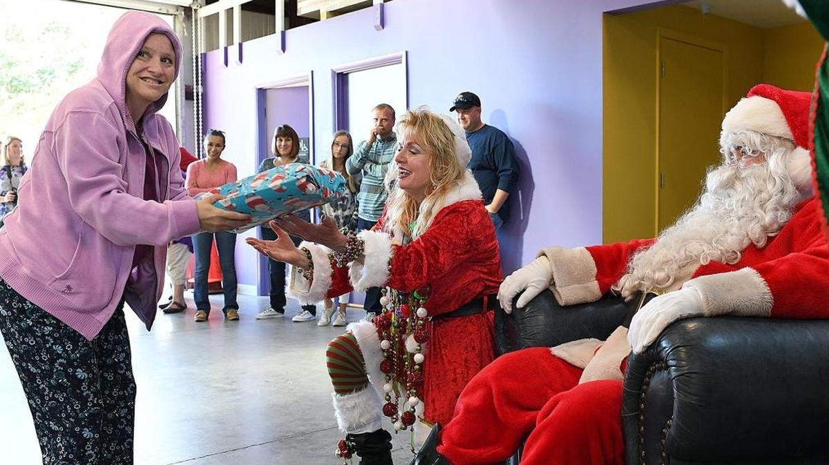 Bradenton firefighter Dana Tindall, dressed as an elf, hands a present to Allison Feathers as they deliver holiday gifts Thursday at The Haven, a non-profit agency serving children, teens, and adults with disabilities in Sarasota.