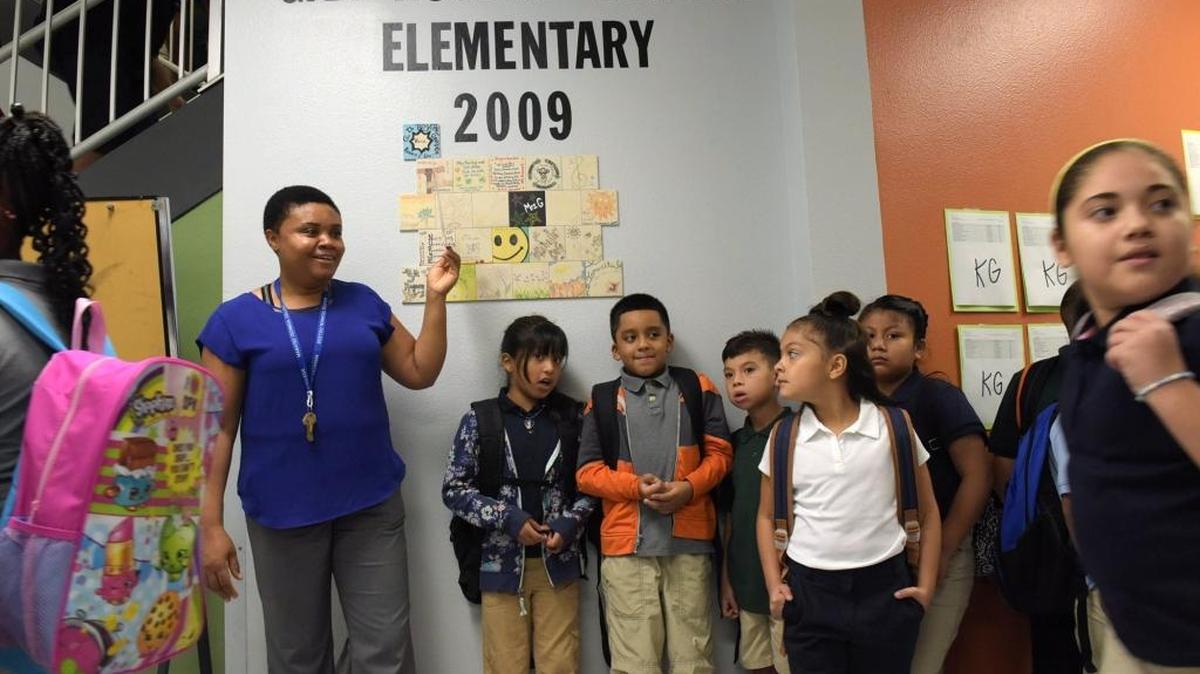 Third-grade teacher Ermite Constant holds up a sign for her students at Rogers Garden-Bullock Elementary School on the first day of school.