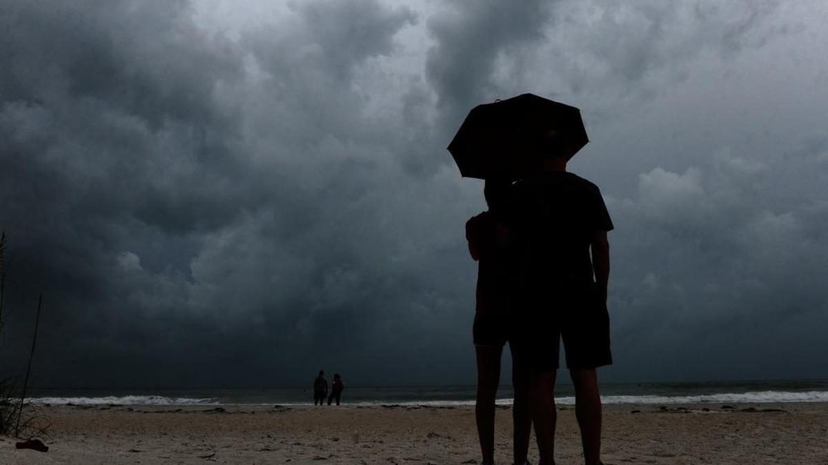 Matthew Wilson holds an umbrella as his wife, Christi, takes photographs of surfers off Cortez Beach on Anna Maria Island on June 6, 2016, as Tropical Storm Colin moves its way across the Gulf of Mexico toward Florida.